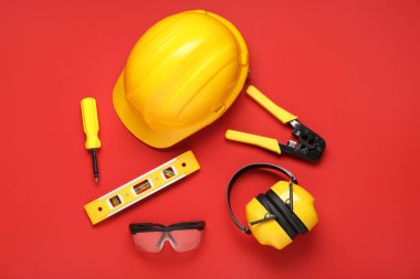 Kırmızı arka planda şapkalar, inşaat aletleri ve koruyucu kulaklıklar.