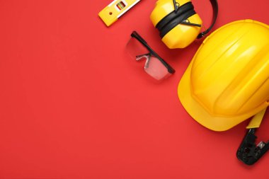 Sert şapkalar, güvenlik gözlükleri ve kırmızı arka planda koruyucu kulaklıklar.