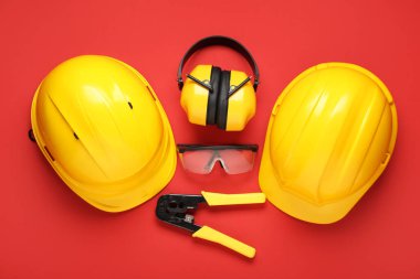 Sert şapkalar, güvenlik gözlükleri ve kırmızı arka planda koruyucu kulaklıklar.