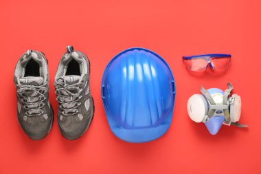 Sert şapka, solunum cihazı, güvenlik gözlükleri ve kırmızı arka planda botlar.