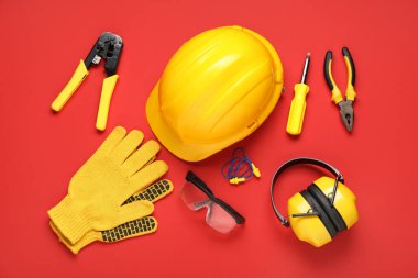 Kırmızı arka planda şapkalar, inşaat aletleri ve koruyucu kulaklıklar.
