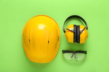 Koruyucu kulaklıkları ve yeşil arka planda güvenlik gözlüğü olan sert şapka.