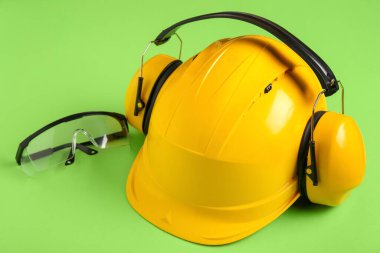 Koruyucu kulaklıkları ve yeşil arka planda güvenlik gözlüğü olan sert şapka.
