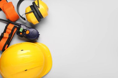 Koruyucu kulaklıkları, emniyet kemerleri ve gri arka planda radyo vericisi olan bir şapka.