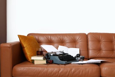 Klasik daktilo, fotoğraf makinesi ve oturma odasındaki kahverengi deri koltukta kitaplar.