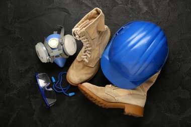 Botlu sert şapka, solunum cihazı ve siyah grunge arka planda güvenlik gözlüğü.