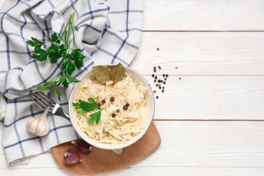 Lezzetli lahana turşulu kase ve beyaz ahşap arka planda farklı baharatlar.