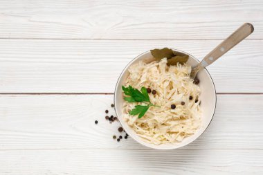 Lezzetli lahana turşulu kase ve beyaz ahşap arka planda farklı baharatlar.