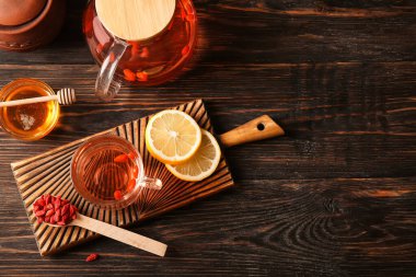 Bir bardak limonlu sıcak goji çayı ve ahşap arka planda bir kase bal.