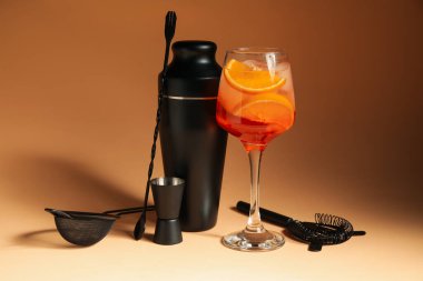 Bir bardak Aperol sprey kokteyli ve bej arka planda barmen aletleri.