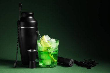 Yeşil arka planda bir bardak taze kokteyl ve barmen aletleri.