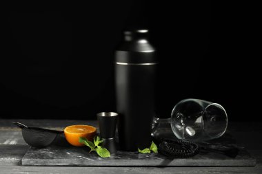 Barmen seti ve kokteyl malzemeleri siyah duvarın yanındaki gri ahşap masada.