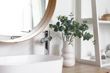 Yapay okaliptüs dalları olan ve şifoniyere batan şık bir banyo.