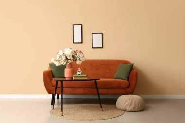 Kahverengi kanepesi ve kahve masasında suni çiçekleri olan şık bir oturma odası.