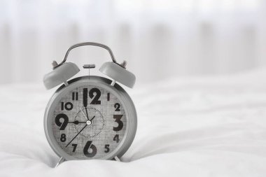 Yataktaki gri çalar saat, aydınlık yatak odasında, yakın plan.