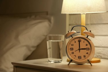Çalar saat, parlayan lamba ve karanlık yatak odasındaki masada bir bardak su.