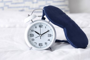 Çalar saat ve uyku maskesi açık yatak odasında, yakın plan.