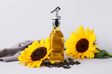 Gri zemin üzerinde ayçiçeği ve tohumları olan bir şişe yağ.