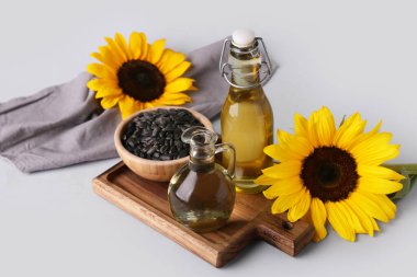 Gri arka planda ayçiçekleri, tohumlar, şişe ve sürahi yağ