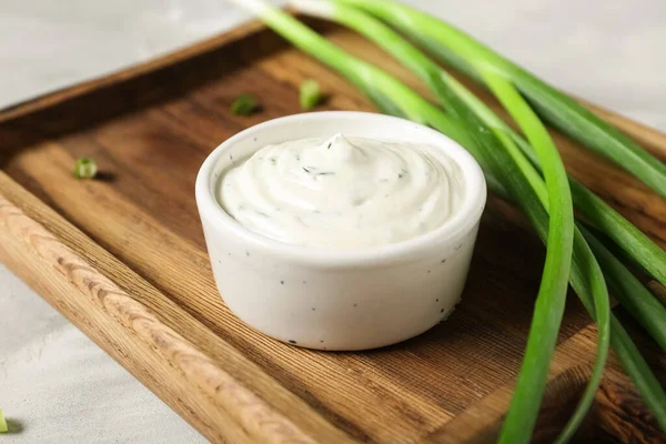 Lezzetli ekşi krema ve gri grunge masasında taze yeşil soğanla kesme tahtası.