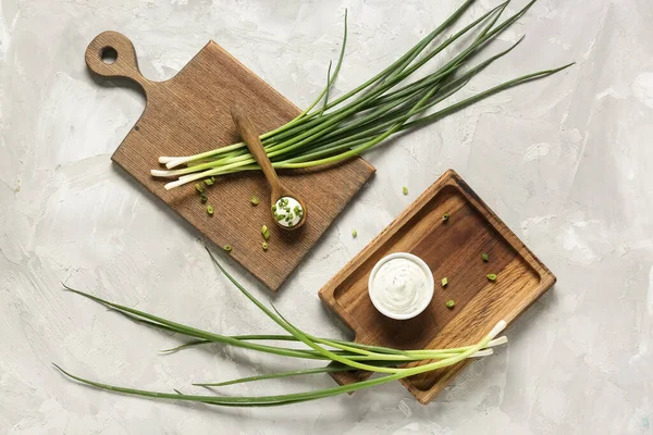 Tabak ve kaşık dolusu ekşi krema ve grunge masasında doğranmış yeşil soğan dilimleme tahtaları.