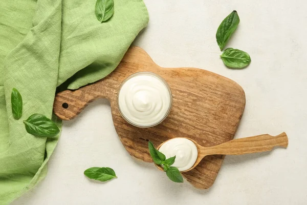 Kase ve bir kaşık ekşi krema ve beyaz grunge masasında taze fesleğen ile kesme tahtaları.