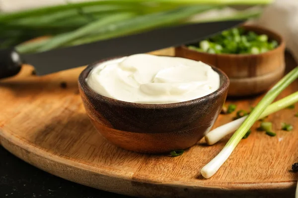 Lezzetli ekşi krema ve siyah grunge masasında yeşil soğan.
