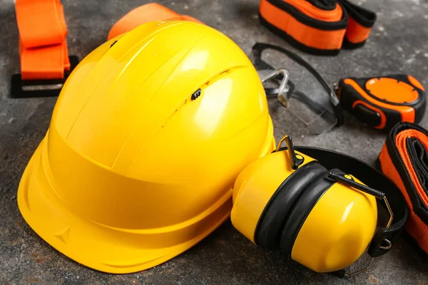 Sert şapka, koruyucu kulaklıklar ve gri grunge arka planda emniyet kemerleri.