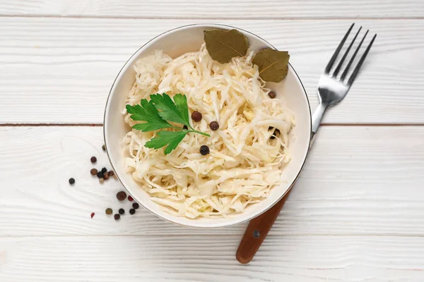 Lezzetli lahana turşulu kase ve beyaz ahşap arka planda farklı baharatlar.