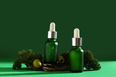 Yeşil zemin üzerinde gerekli yağ şişeleri, ağaç kabuğu, yosun ve zeytin içeren kompozisyon, yakın plan