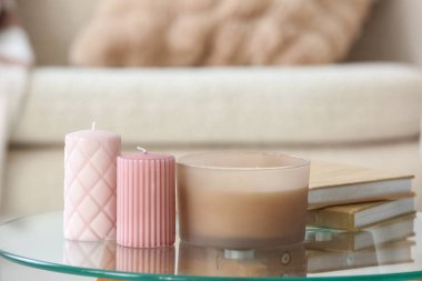 Kitaplar ve farklı mumlar oturma odasındaki cam masada, yakın plan.