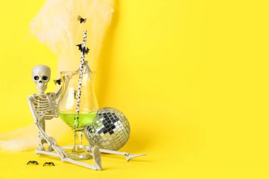 Disko topu, iskelet ve sarı arka planda Cadılar Bayramı dekoru olan lezzetli bir kokteyl.