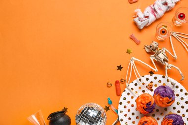 Disko topu, shot bardakları, yarasa iskeleti ve turuncu arka planda Cadılar Bayramı dekoru olan lezzetli kekler.