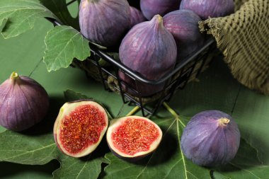 Taze incirli metal sepet ve yeşil ahşap arka planda yapraklar, yakın plan.