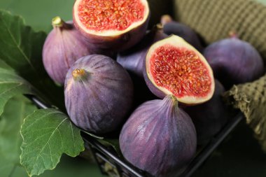 Taze incirli metal sepet ve yeşil ahşap arka planda yapraklar, yakın plan.