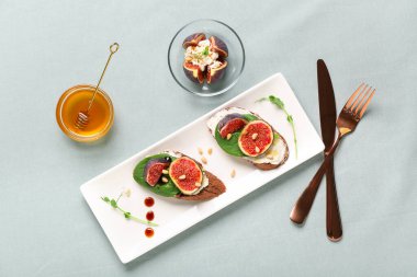 Arka plan olarak gri kumaş üzerine taze incir konmuş bir tabak sandviç.