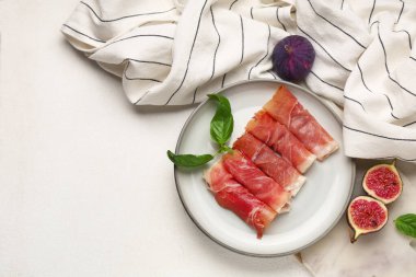 Lezzetli prosciutto dilimleri, fesleğen yaprakları ve beyaz arka planda taze incir tabakları.