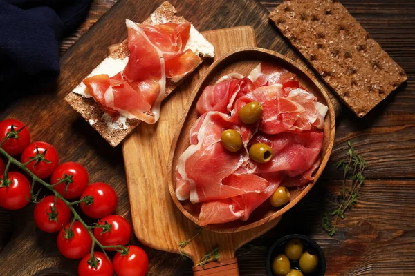 Nefis prosciutto dilimleri, zeytin ve ahşap zemin üzerinde kiraz domatesli tabak.