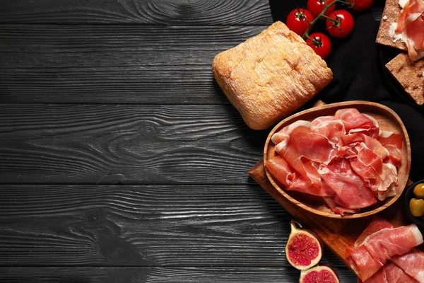 Lezzetli prosciutto dilimleri, siyah ahşap arka planda incir ve ciabatta.