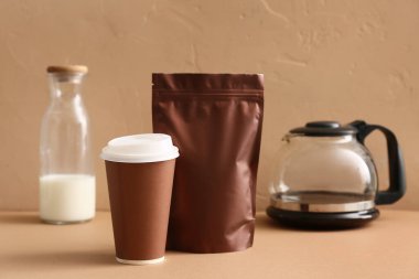 Kahverengi çanak kahve demliği, kağıt bardak ve renkli bir şişe süt.