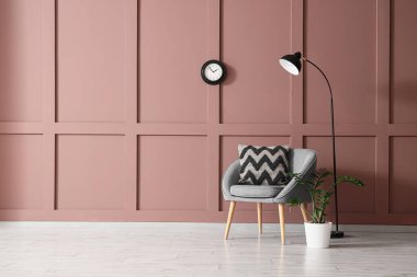 Yumuşak yastıklı rahat gri koltuk ve oturma odasındaki kahverengi duvarın yanındaki lamba.