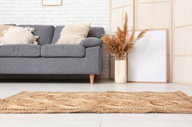 Oturma odasının içinde kanepe, katlanan ekran, kuru çiçekler ve beyaz tuğla duvarın yanında hasır bir halı.