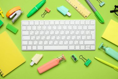 Yeşil arkaplanda bilgisayar klavyesi ve farklı kırtasiye malzemesi olan kompozisyon