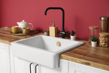 Modern mutfağın iç kısımlarında kırmızı duvarın yanında ev bitkileri, çaydanlık ve fincanlar olan beyaz tezgahlar, yakın plan.