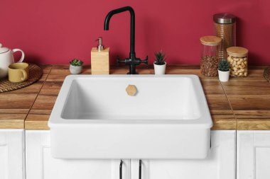 Beyaz tezgahlar ev bitkileriyle dolu, kavanozlar ise kırmızı duvarın yanında modern mutfağın içinde, yakın plan.