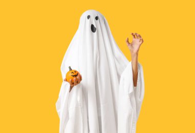 Cadılar Bayramı 'nda hayalet gibi giyinmiş genç çocuk sarı arka planda balkabağıyla