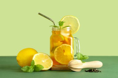 Limonlu bir kavanoz meyve çayı, ahşap sıkacağı ve yeşil arka planda kuru yapraklar.