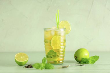 Yeşil zemin üzerinde limon dilimleri ve nane yapraklarıyla bir bardak soğuk çay.