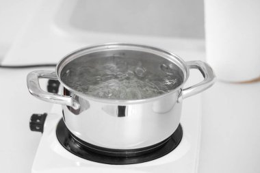 Mutfaktaki küçük ocağın üstünde kaynar su bulunan paslanmaz çelik tencereye yakın çekim.