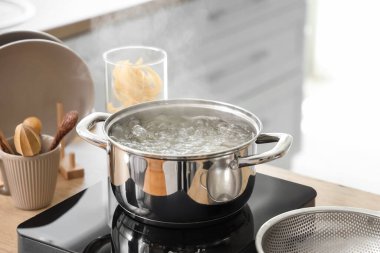 Mutfaktaki ocağın üstünde kaynar su bulunan paslanmaz çelik tencere, yakın plan.